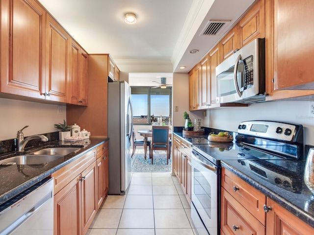 kitchen featuring sink, dark stone countertops, light tile patterned floors, ornamental molding, and appliances with stainless steel finishes