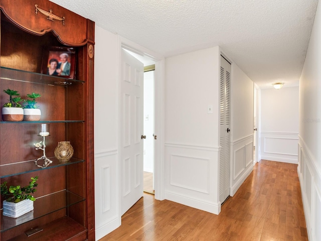 corridor with a textured ceiling and light wood-type flooring