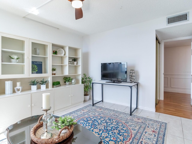 living room featuring ceiling fan, light tile patterned flooring, and a textured ceiling