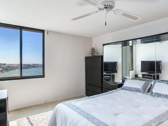 bedroom featuring carpet, ceiling fan, a water view, and a textured ceiling