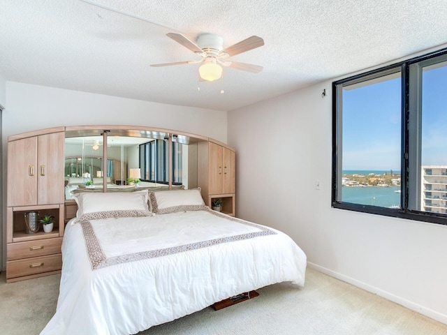 carpeted bedroom with ceiling fan, a water view, and a textured ceiling