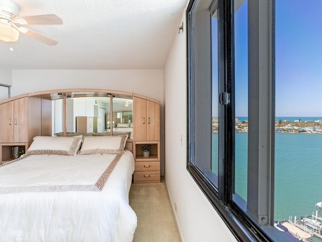 carpeted bedroom featuring ceiling fan, a water view, and a textured ceiling