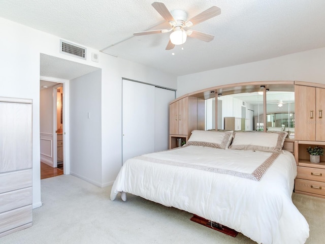 bedroom featuring a textured ceiling, ceiling fan, light carpet, and a closet