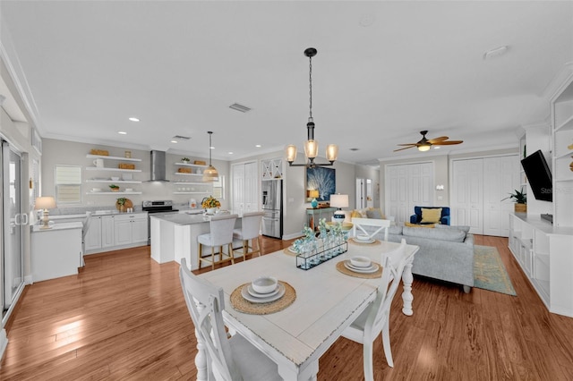 dining room with ceiling fan with notable chandelier, light hardwood / wood-style flooring, and ornamental molding