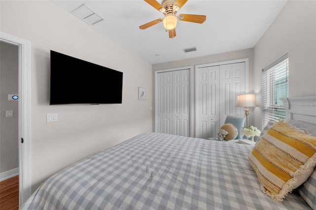 bedroom featuring hardwood / wood-style floors, ceiling fan, and multiple closets