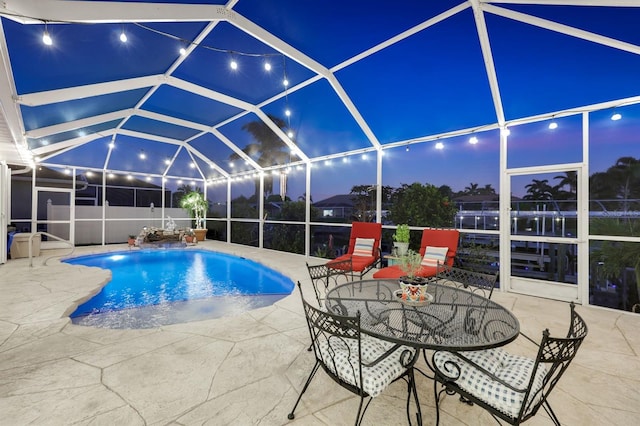 pool at twilight with glass enclosure and a patio area