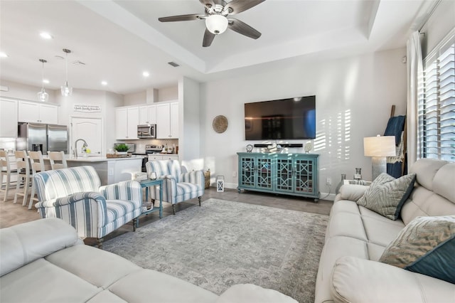 living room featuring ceiling fan and a raised ceiling