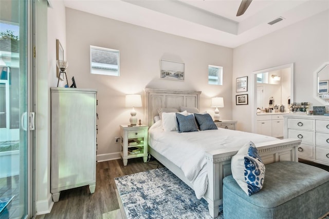 bedroom with a raised ceiling, ensuite bathroom, ceiling fan, and dark hardwood / wood-style flooring