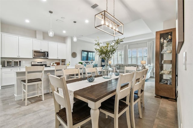 dining area with a tray ceiling, visible vents, and recessed lighting