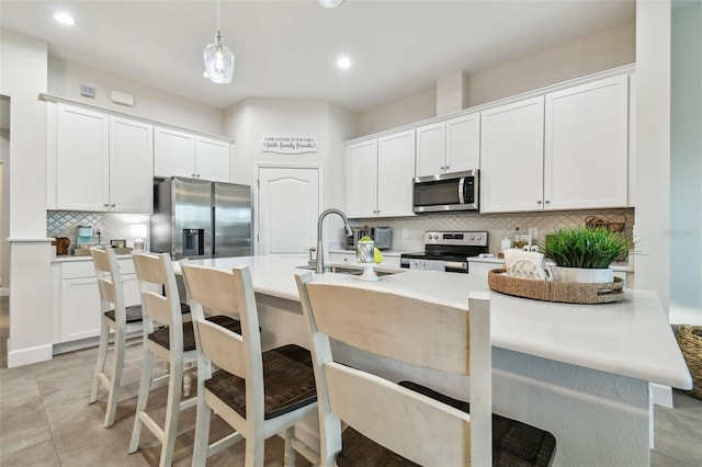 kitchen with appliances with stainless steel finishes, a breakfast bar area, light countertops, white cabinetry, and pendant lighting