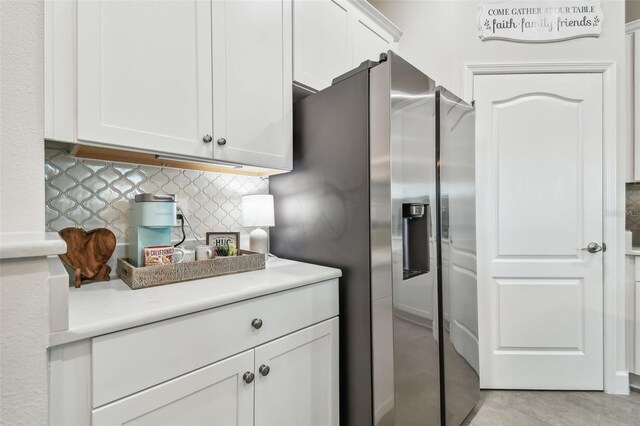 kitchen with light countertops, tasteful backsplash, stainless steel fridge, and white cabinets