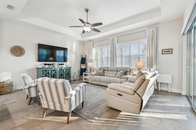 tiled living room featuring baseboards, visible vents, a raised ceiling, and a ceiling fan