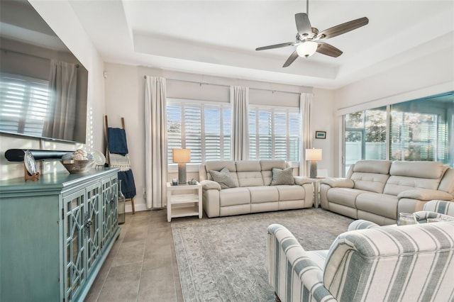 living area featuring ceiling fan, a tray ceiling, a wealth of natural light, and baseboards