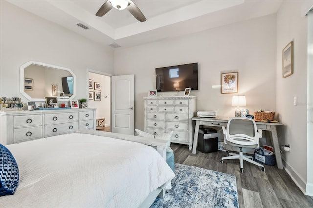 bedroom featuring a tray ceiling, visible vents, a ceiling fan, wood finished floors, and baseboards