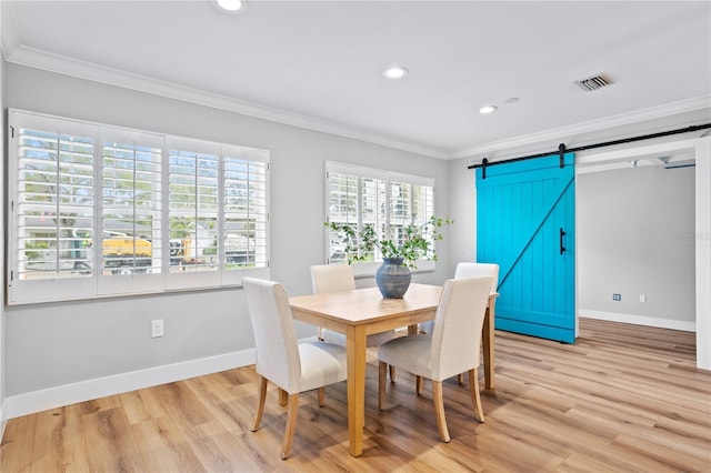 dining area with light hardwood / wood-style floors, ornamental molding, and a barn door