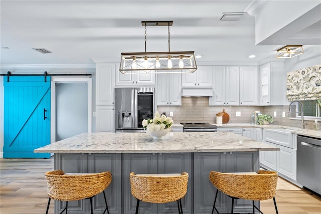 kitchen featuring a kitchen island, stainless steel appliances, hanging light fixtures, light stone counters, and a barn door