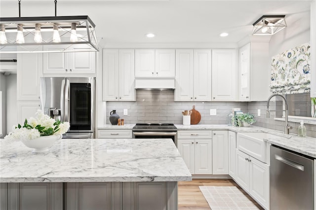 kitchen featuring decorative light fixtures, white cabinetry, stainless steel appliances, light stone counters, and light hardwood / wood-style flooring