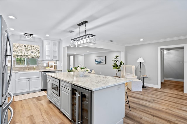 kitchen featuring white cabinets, beverage cooler, appliances with stainless steel finishes, a kitchen island, and a breakfast bar area