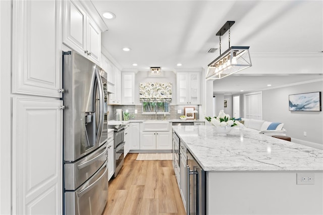 kitchen featuring light stone counters, white cabinets, appliances with stainless steel finishes, and crown molding