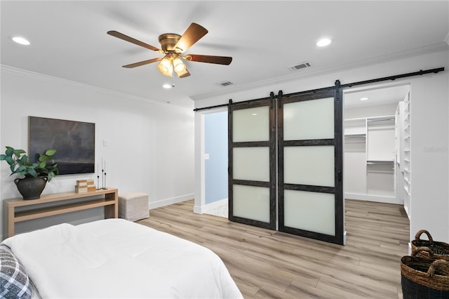 bedroom with a spacious closet, a barn door, a closet, ornamental molding, and ceiling fan