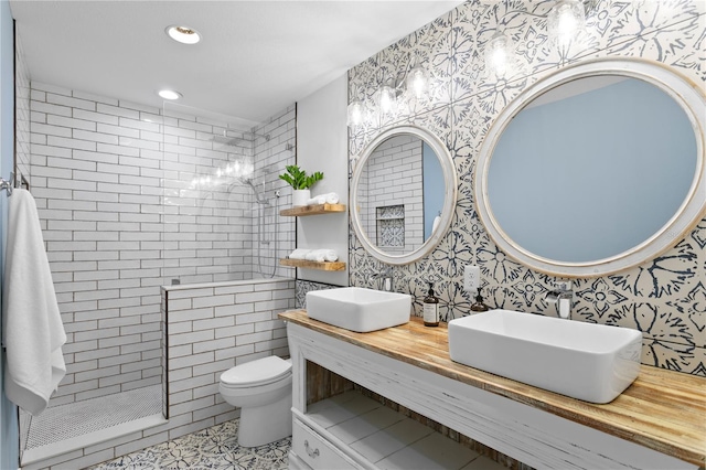 bathroom with toilet, vanity, a tile shower, and tile patterned flooring