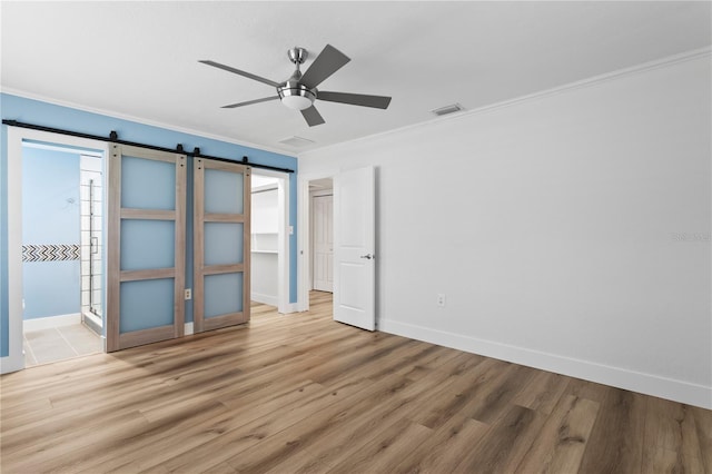 unfurnished bedroom with a closet, ornamental molding, light wood-type flooring, ceiling fan, and a barn door