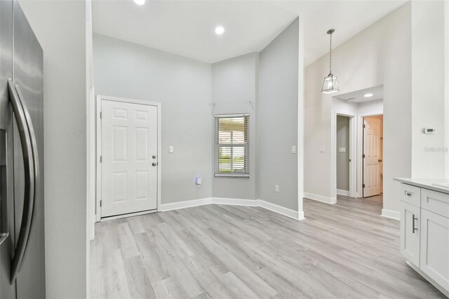 kitchen with stainless steel fridge, decorative light fixtures, light hardwood / wood-style flooring, white cabinets, and a high ceiling