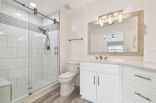 bathroom featuring ceiling fan, toilet, vanity, a shower with shower door, and hardwood / wood-style flooring