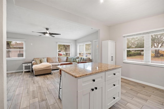 kitchen with a center island, light stone counters, white cabinetry, and a healthy amount of sunlight