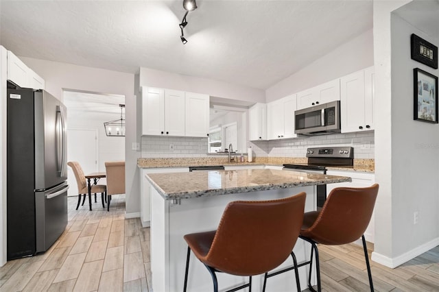 kitchen with a center island, light stone countertops, appliances with stainless steel finishes, a kitchen bar, and white cabinetry