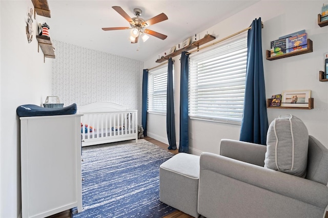 bedroom featuring ceiling fan, dark hardwood / wood-style floors, and a crib