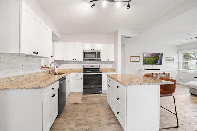 kitchen with sink, a center island, a kitchen bar, white cabinets, and appliances with stainless steel finishes