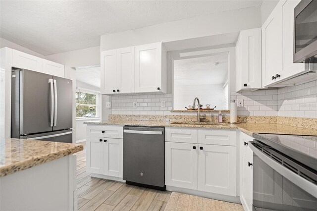 kitchen featuring white cabinets, sink, decorative backsplash, light stone countertops, and stainless steel appliances