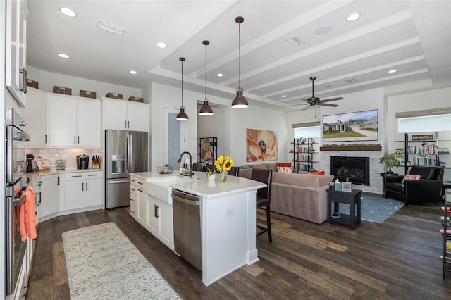 kitchen featuring ceiling fan, stainless steel appliances, decorative light fixtures, a center island with sink, and white cabinets