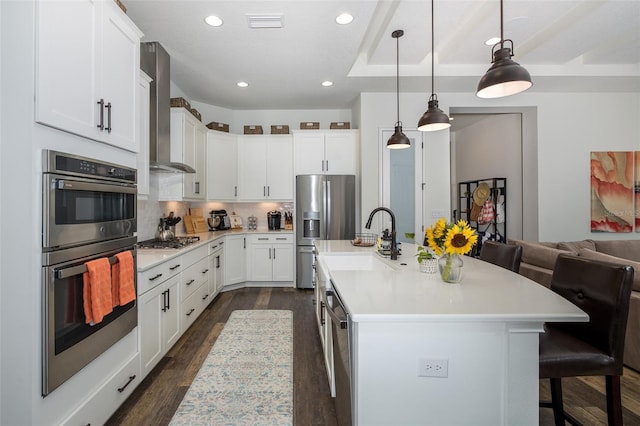 kitchen with wall chimney exhaust hood, a breakfast bar, decorative light fixtures, a center island with sink, and white cabinets