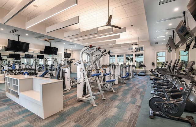 gym featuring dark colored carpet, a towering ceiling, and ceiling fan