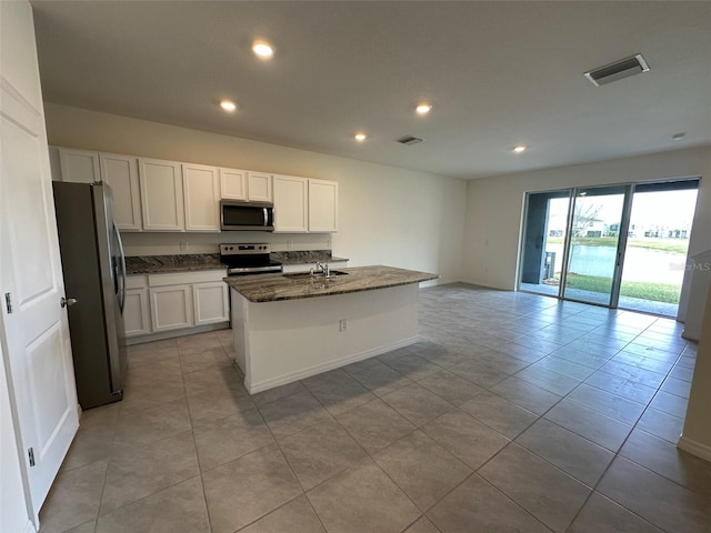 kitchen featuring white cabinets, appliances with stainless steel finishes, a center island with sink, and dark stone counters