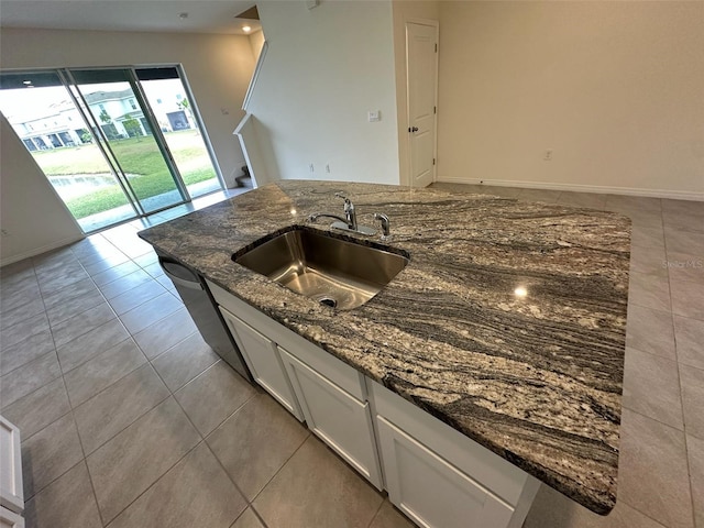 kitchen with light tile patterned floors, white cabinetry, dark stone counters, and sink