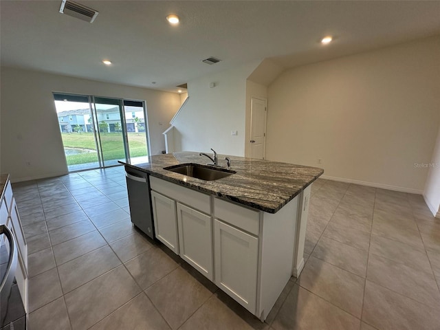 kitchen with stainless steel dishwasher, dark stone counters, sink, white cabinets, and an island with sink