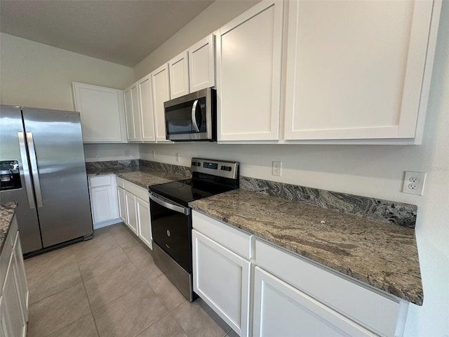 kitchen with light tile patterned floors, white cabinetry, appliances with stainless steel finishes, and dark stone counters