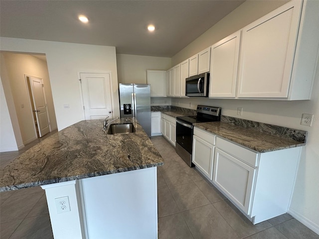 kitchen with a center island with sink, white cabinets, sink, dark tile patterned floors, and appliances with stainless steel finishes