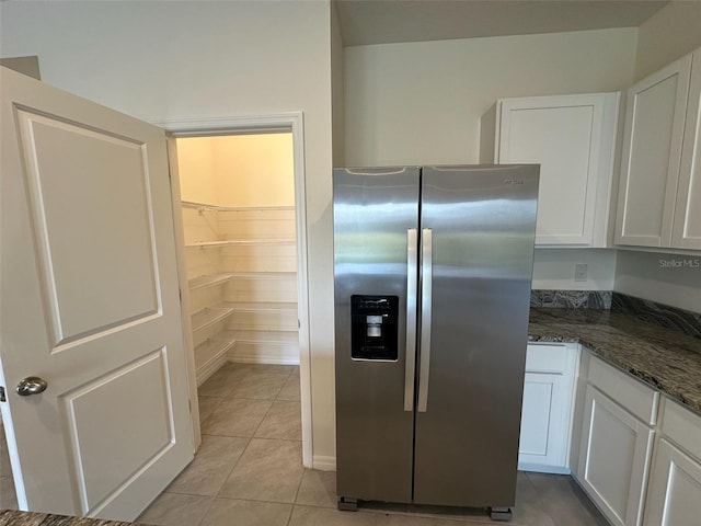 kitchen with light tile patterned flooring, white cabinets, dark stone counters, and stainless steel refrigerator with ice dispenser