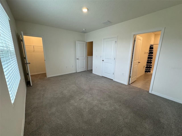 unfurnished bedroom featuring carpet, a walk in closet, a textured ceiling, and a closet