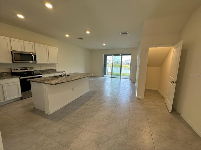 kitchen with sink, stainless steel appliances, dark stone counters, a center island with sink, and white cabinets