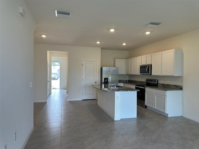 kitchen featuring dark stone counters, a kitchen island with sink, white cabinets, and stainless steel appliances