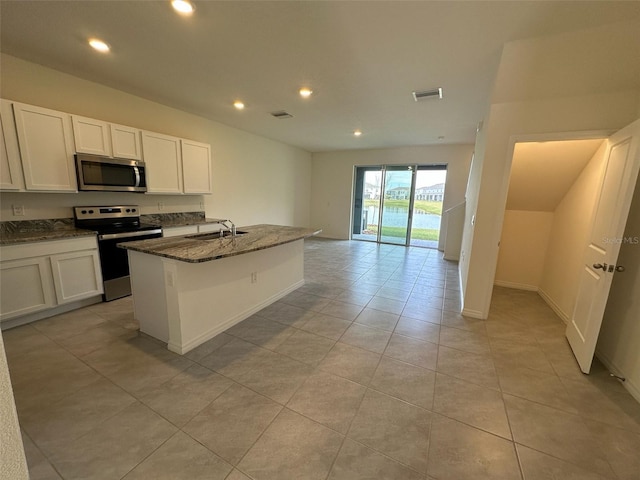 kitchen with a center island with sink, white cabinetry, stainless steel appliances, and dark stone counters