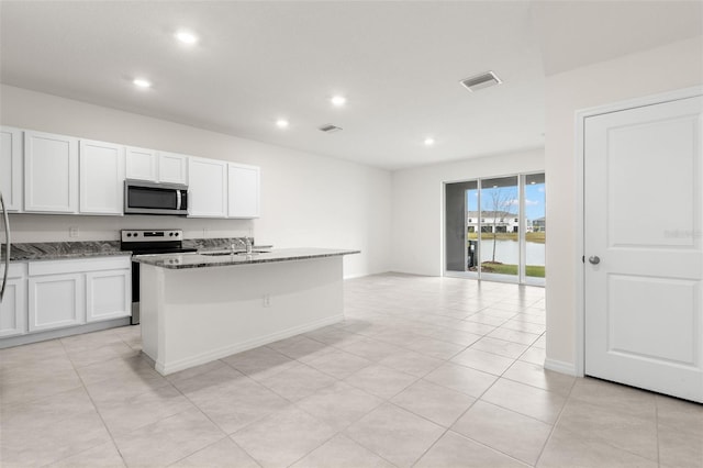 kitchen with appliances with stainless steel finishes, stone countertops, an island with sink, white cabinets, and light tile patterned floors