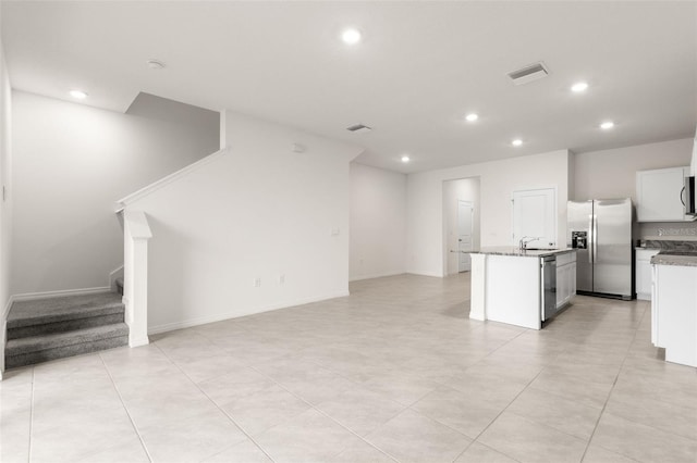 kitchen featuring white cabinetry, light stone counters, stainless steel appliances, and a center island with sink