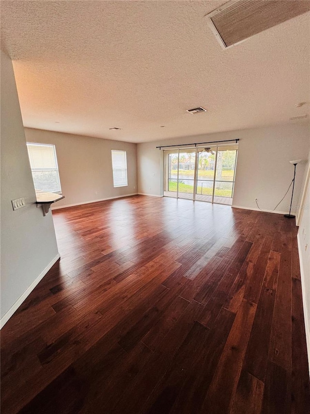 empty room featuring a textured ceiling, a healthy amount of sunlight, and dark wood-type flooring