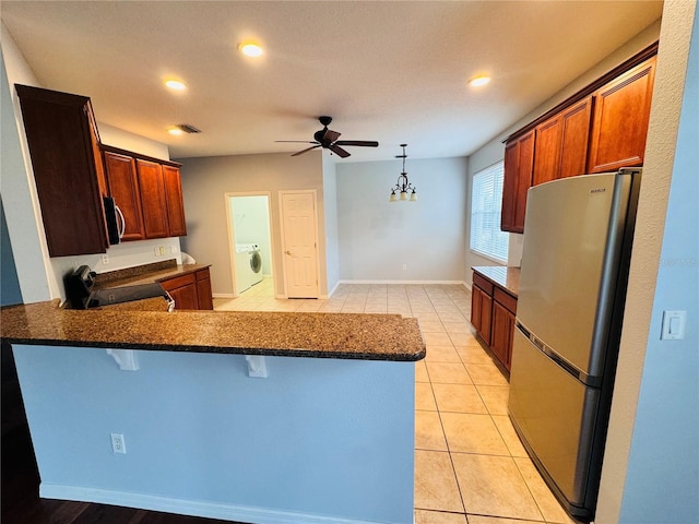 kitchen featuring kitchen peninsula, a breakfast bar, ceiling fan with notable chandelier, stainless steel appliances, and washer / dryer